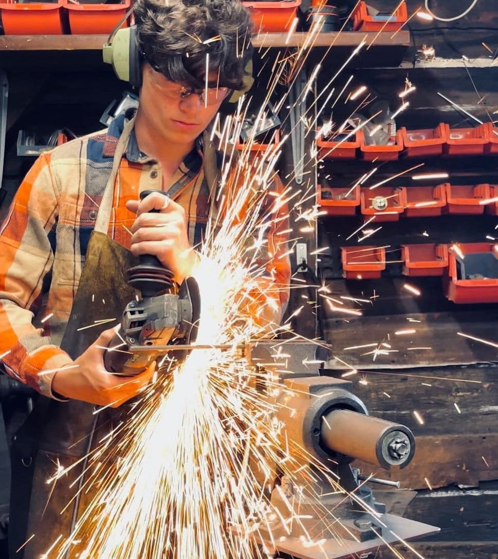 Judson grinding a forged piece, sparks arcing across the shop